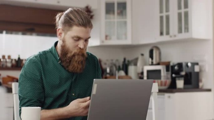 男人在厨房里使用笔记本电脑和电话