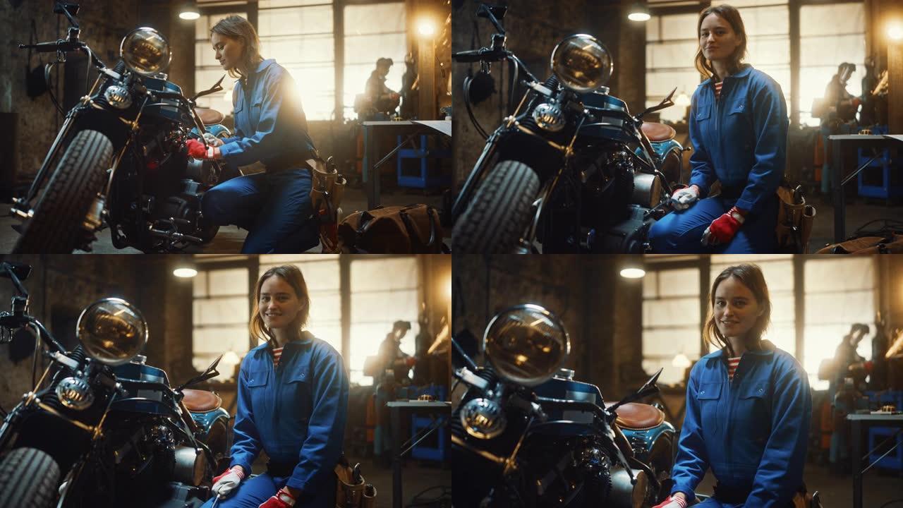 年轻漂亮的女机械师正在设计一辆定制的Bobber摩托车。穿着蓝色连体裤的天才女孩。她转身对着镜头微笑