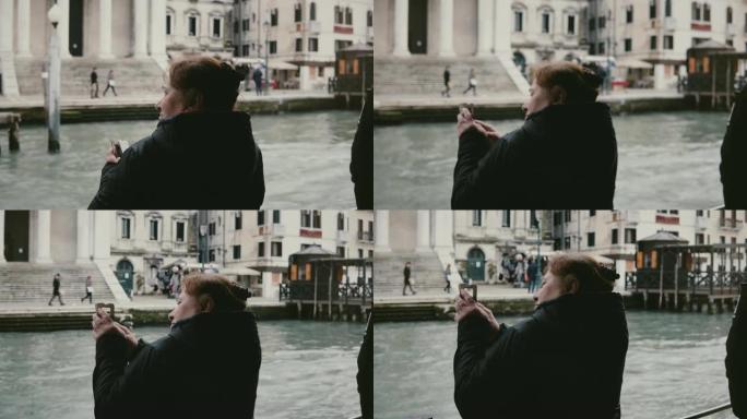 后视图兴奋的活跃的白人老年旅游妇女在威尼斯之旅的贡多拉游览中拍摄智能手机照片。