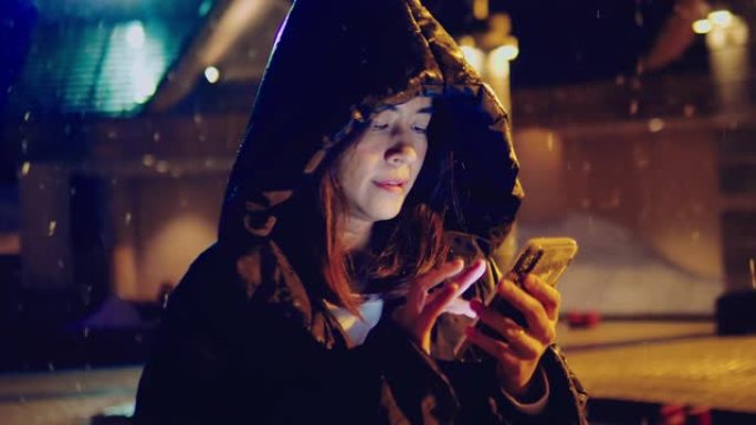 带手机的年轻亚洲女孩在带圣诞灯的冬季街道上