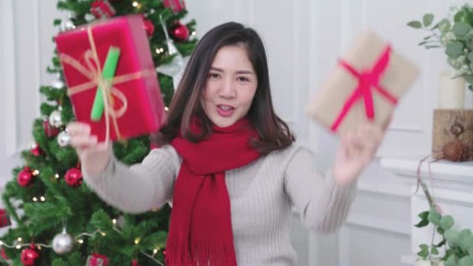 年轻的亚洲女孩拿着礼物在客厅对着相机展示圣诞活动。