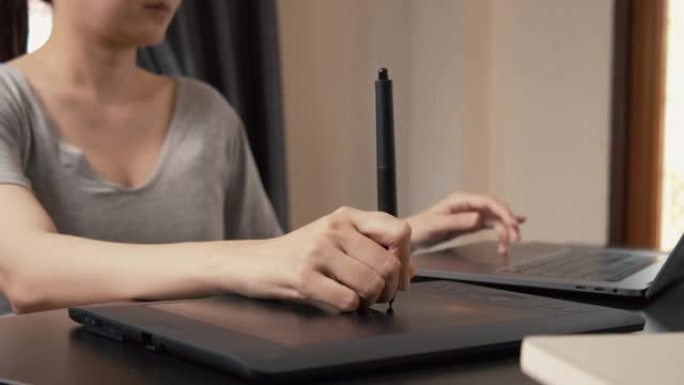亚洲女性专业平面设计师使用笔记本电脑和数字平板电脑在家庭办公室工作。创意，灵感在家远程工作。