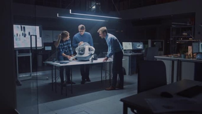 深夜在机器人工程设施中，三名技术工程师交谈并研究轮式机器人原型。在后台高科技研究中心，屏幕显示工业设