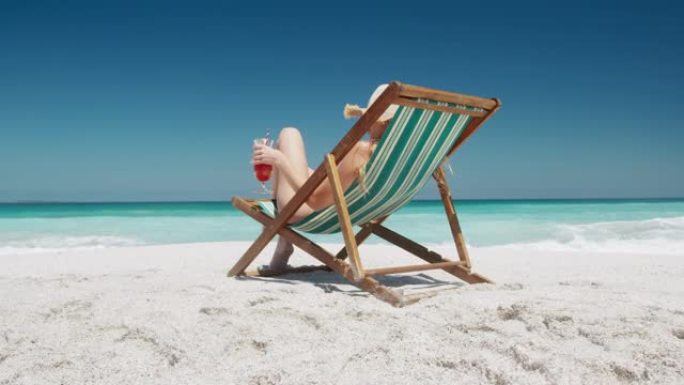 女人在沙滩上的躺椅上喝鸡尾酒