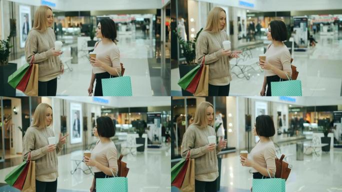 有吸引力的年轻女性在购物中心里聊天，拿着可购买的咖啡和纸袋。人体模型和玻璃墙上的时髦服装是可见的。
