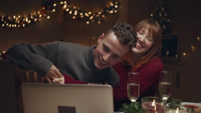 一对年轻夫妇在圣诞节晚上在电脑上浏览照片。他们玩，放纵，玩得开心。