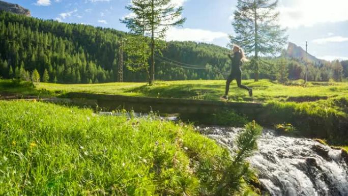 在美丽的晴天，健康的健身女性在大自然中穿过山溪上的一座桥在户外跑步