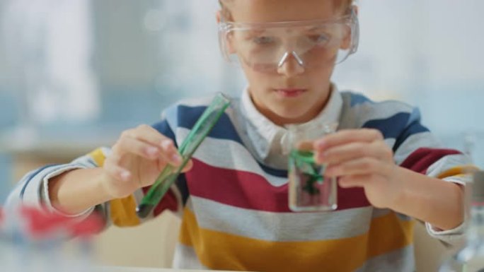 小学科学教室: 戴着安全眼镜的聪明小男孩在烧杯中混合化学物质