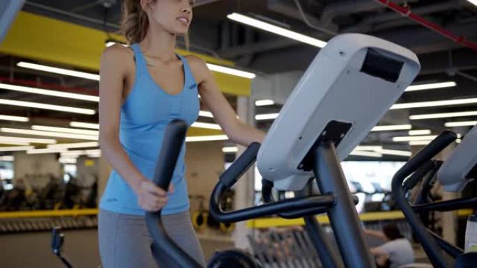 年轻的瘦女人在健身房的椭圆机上锻炼