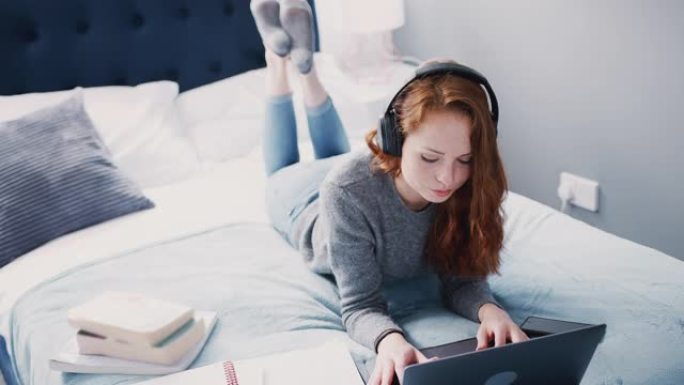 女大学生躺在床上戴着耳机在笔记本电脑上工作-慢动作拍摄