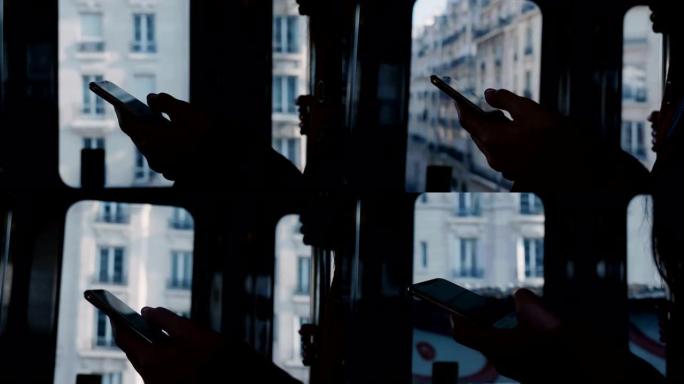 在移动的地铁列车门窗慢动作中，使用智能手机拍摄女性手的深色电影特写剪影。