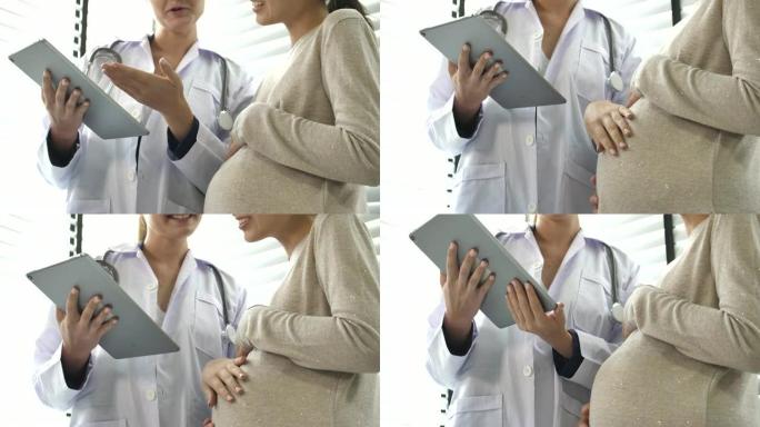 医生使用数字平板电脑并在医院与孕妇交谈