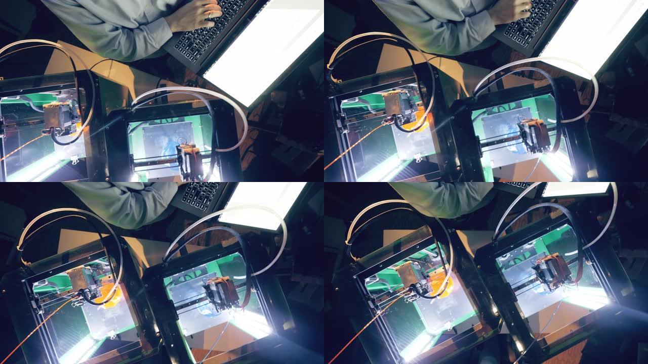 工作中的3d打印机和一个有电脑的人的俯视图。3D打印机从塑料打印对象