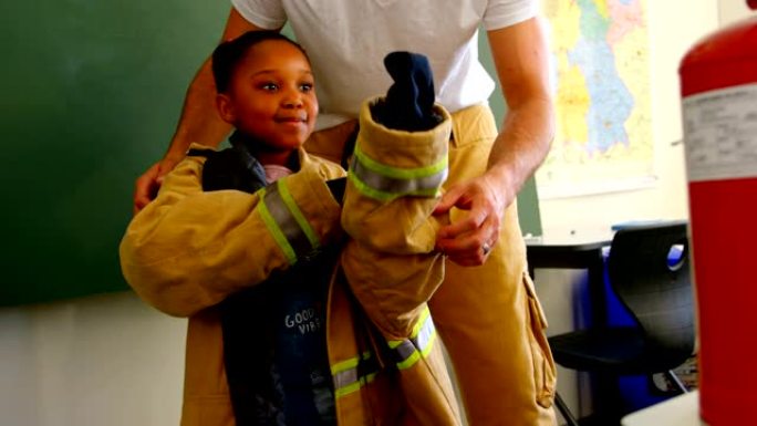 男消防员帮助非裔美国女孩在教室里穿消防制服。女学生微笑