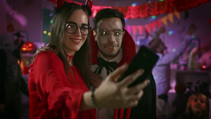 万圣节服装派对: 诱人的她魔鬼和英俊的德古拉伯爵用智能手机为社交网络自拍。在怪物玩得开心的背景组中，