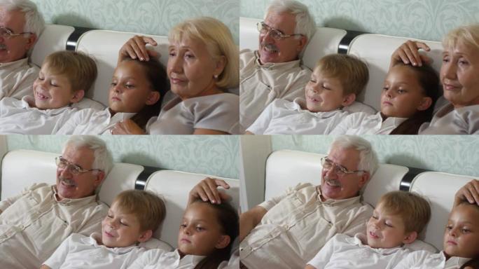 快乐的祖父母和可爱的孙子一起在电视上看电影