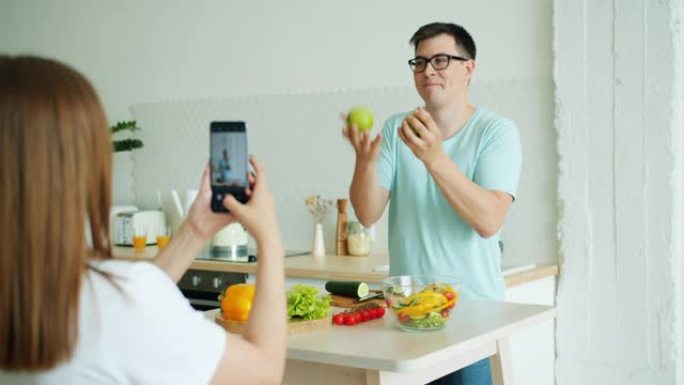 男人在玩苹果，然后在女人拍照时摆姿势为智能手机相机摆姿势