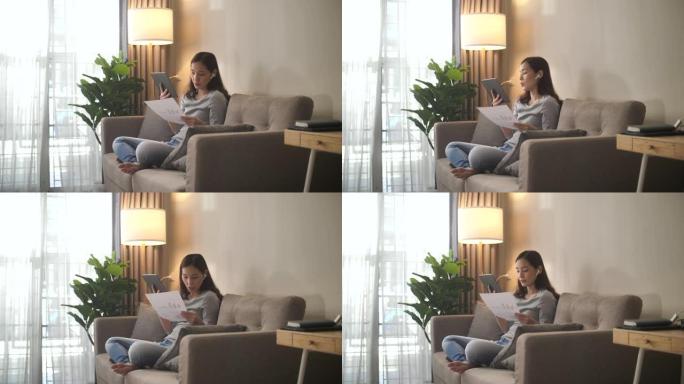 亚洲妇女坐在沙发上，在家中进行视频通话会议