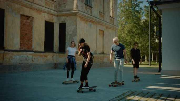 四个很酷的年轻女孩和男孩骑着长板和滑板穿过城市的时尚时髦部分。有吸引力的年轻人在后工业社区玩滑板