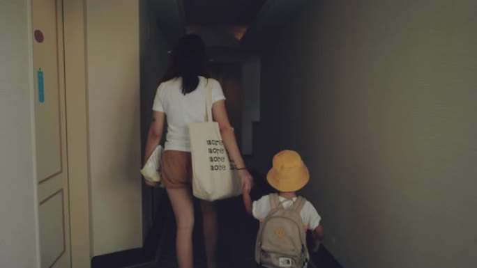 亚洲母亲和她的儿子在酒店的过道上拉着手提箱。