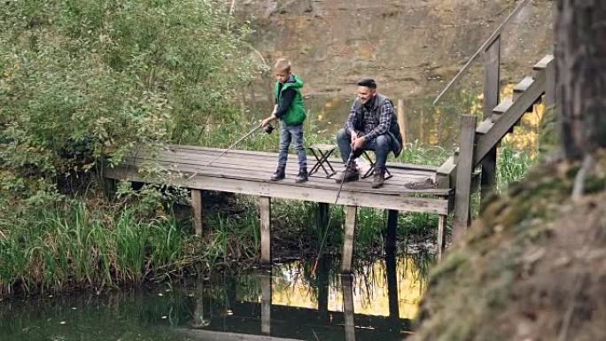 渔夫的儿子可爱的孩子正在和他的父亲从木墩撑杆上钓鱼，而骄傲的父母正在看着他的孩子并与他交谈。父母身份