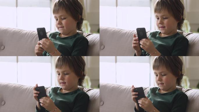 坐在沙发上的可爱小男孩，在家使用智能手机