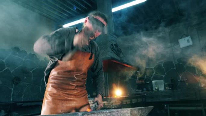 男子在锻造炉工作时用锤子击打金属刀。