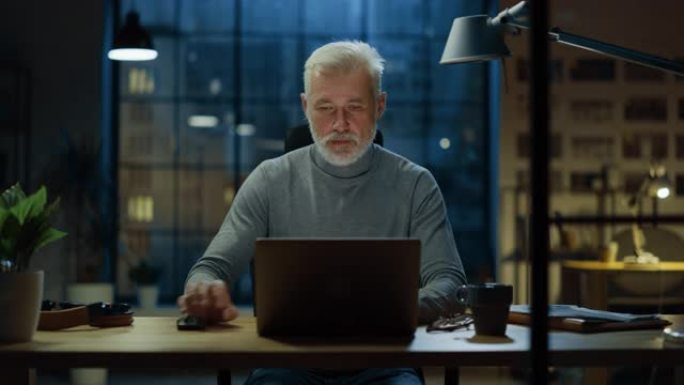 这位英俊而成功的中年大胡子商人在他的办公桌前使用笔记本电脑工作的肖像。在舒适的家庭办公室/工作室工作