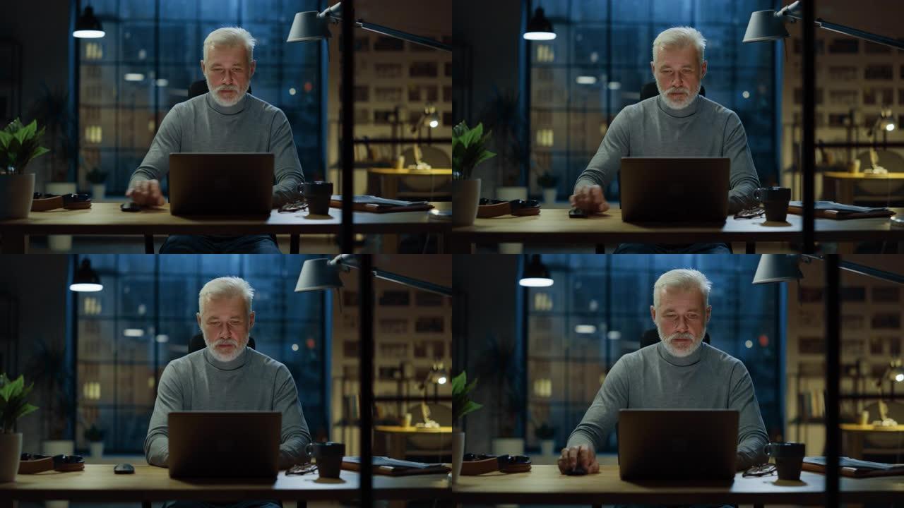 这位英俊而成功的中年大胡子商人在他的办公桌前使用笔记本电脑工作的肖像。在舒适的家庭办公室/工作室工作