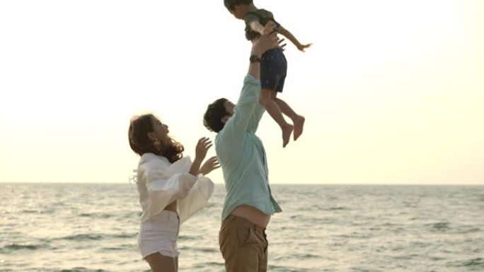 慢动作拍摄快乐的亚洲家庭在日落时在海滩上玩耍，父亲将小男孩抛向空中。