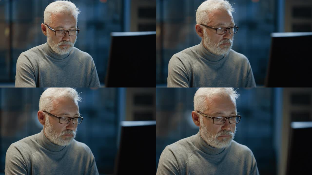 这位英俊而成功的中年大胡子商人在他的办公桌前使用笔记本电脑工作的肖像。对着镜头微笑。晚上在舒适的家庭
