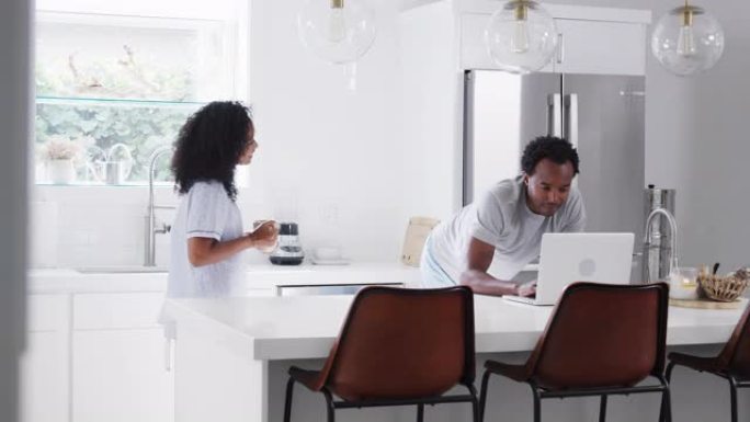 夫妇穿着睡衣站在厨房里用笔记本电脑在家工作
