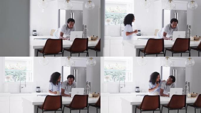 夫妇穿着睡衣站在厨房里用笔记本电脑在家工作