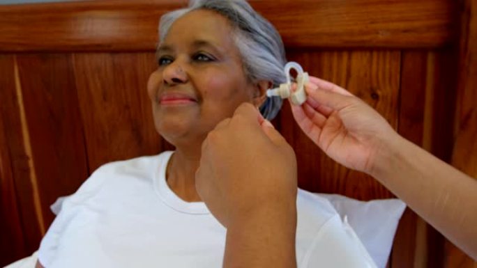 女医生在舒适的家庭4k中插入高级黑人女性耳朵中的助听器
