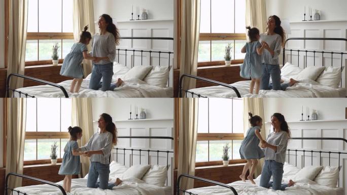 可爱的活跃的小女孩跳到床上和妈妈玩