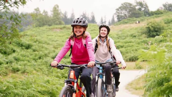 英国湖区野营度假期间，年轻家庭在乡间小路骑山地自行车玩得开心