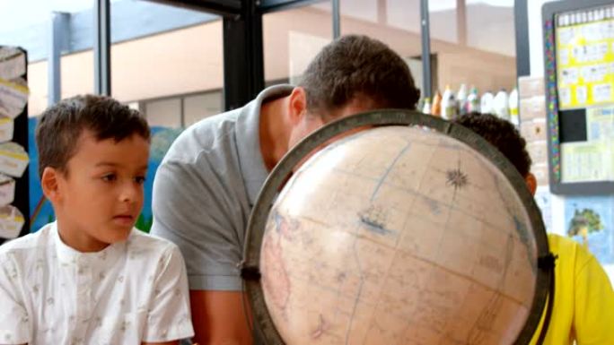 年轻的高加索男老师在4k教室里用地球仪教孩子地理的前视图