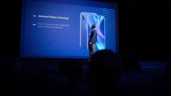 全新产品发布的现场活动: 主旨演讲者向观众展示智能手机设备。电影院屏幕显示具有高端功能和顶级亮点的模