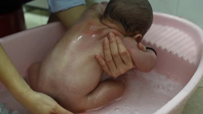 一位亚洲华裔母亲在塑料儿童浴缸的浴室里为男婴洗澡