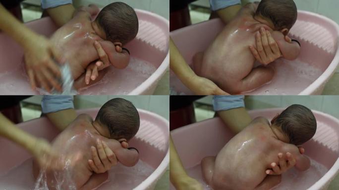 一位亚洲华裔母亲在塑料儿童浴缸的浴室里为男婴洗澡