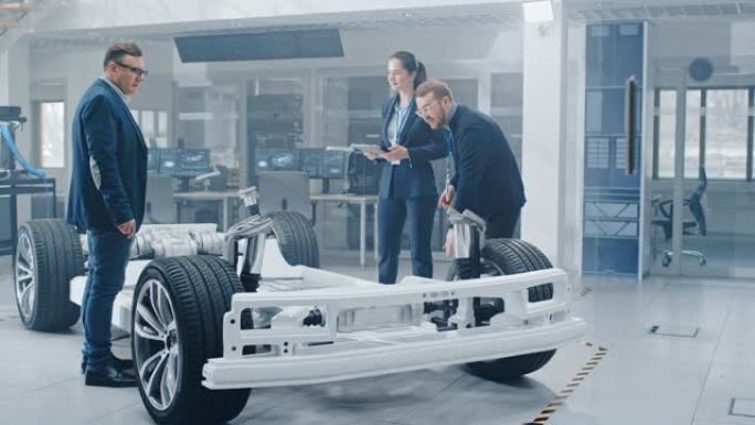 汽车设计工程师在研究电动汽车底盘原型时交谈。在创新实验室设施概念车辆框架包括车轮，悬架，发动机和电池