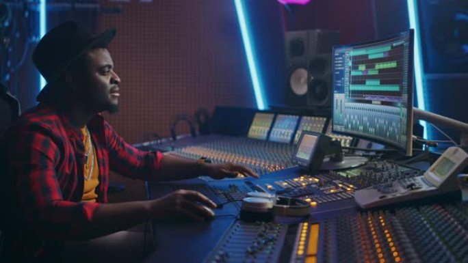 时尚的音频工程师/制作人在音乐录音棚工作，使用混音板和软件来创作现代热门歌曲。黑人艺术家音乐家使用控