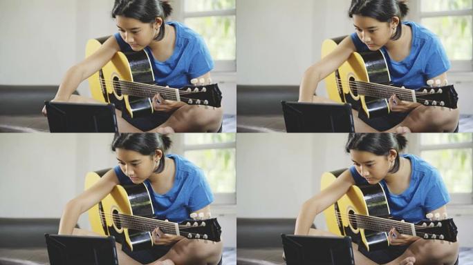 亚洲年轻女孩在平板电脑上学习在线吉他课