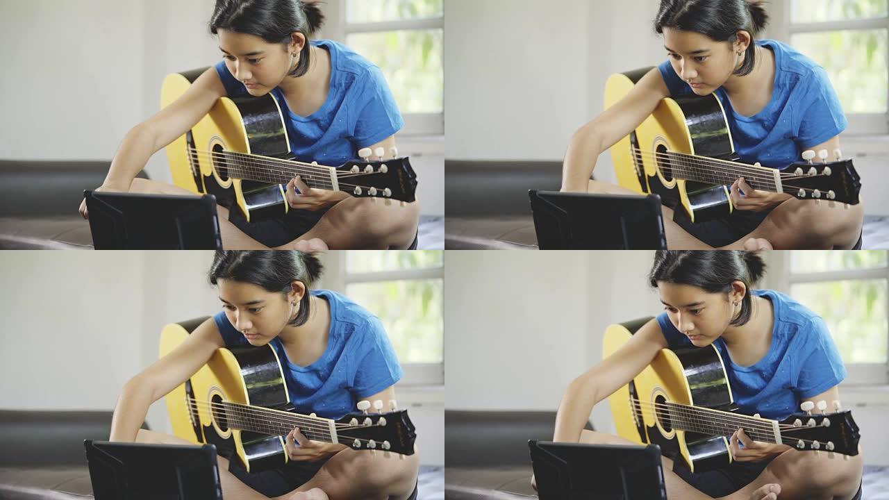 亚洲年轻女孩在平板电脑上学习在线吉他课