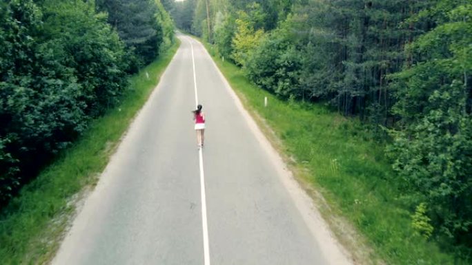 鸟瞰图的森林道路和一个苗条的年轻女子在其中奔跑