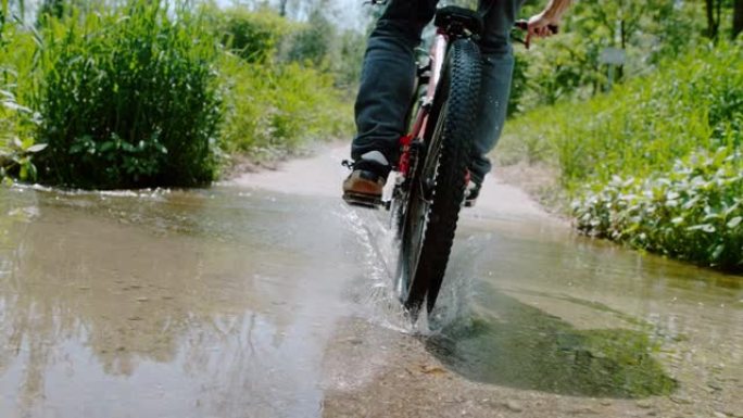 SLO MO骑自行车的人在一条土路上跳入水坑