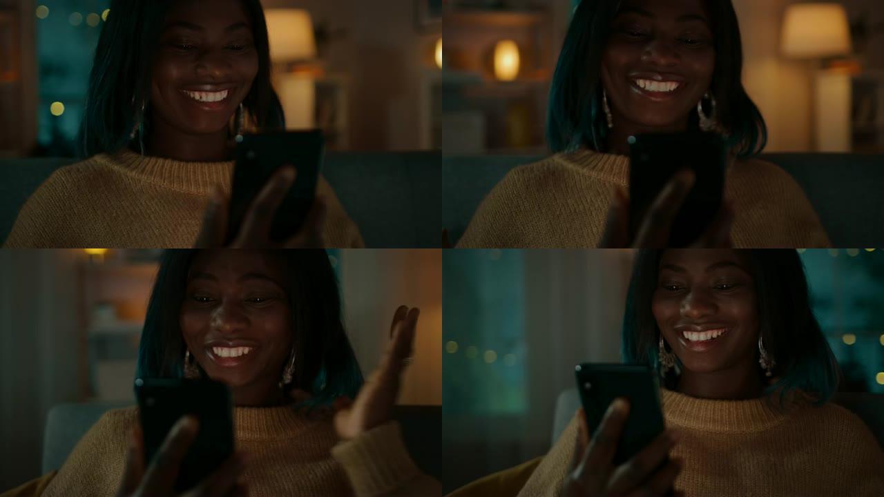 美丽的黑人女孩的肖像坐在家里的沙发上时使用智能手机，她与朋友进行视频通话并与他们聊天。在可爱的女人微