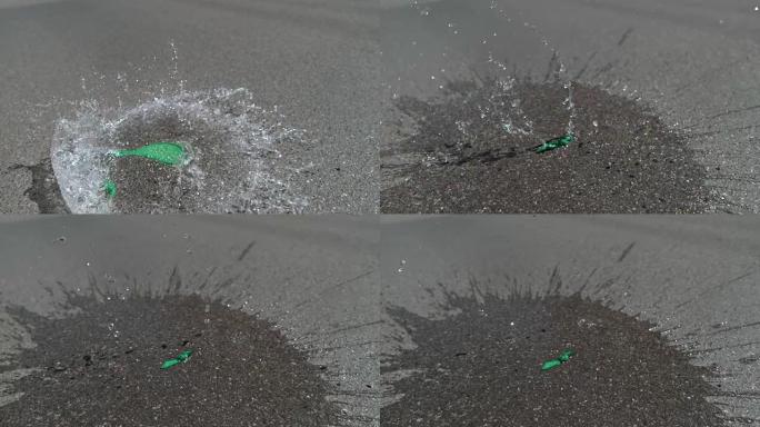 慢动作: 装满水的绿色气球落在沥青路面上并弹出。