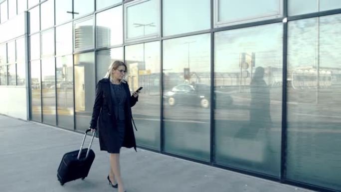 带着智能手机和手提箱的女商人在机场人行道上行走