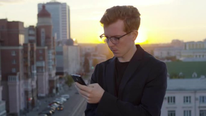年轻人在日落时在屋顶上的智能手机上打字
